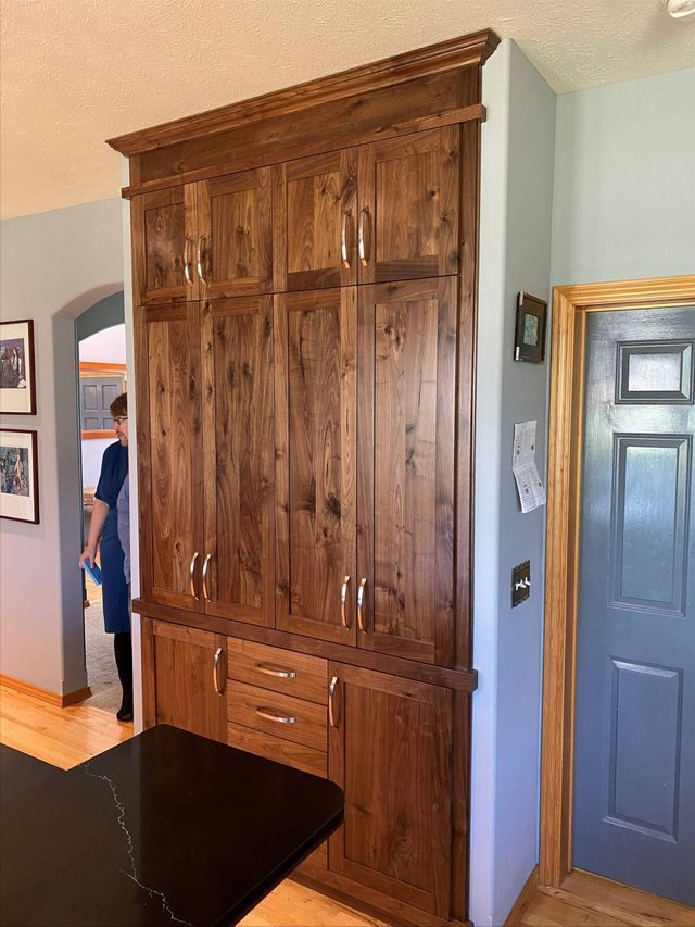 A woman is standing in a kitchen next to a large wooden cabinet.