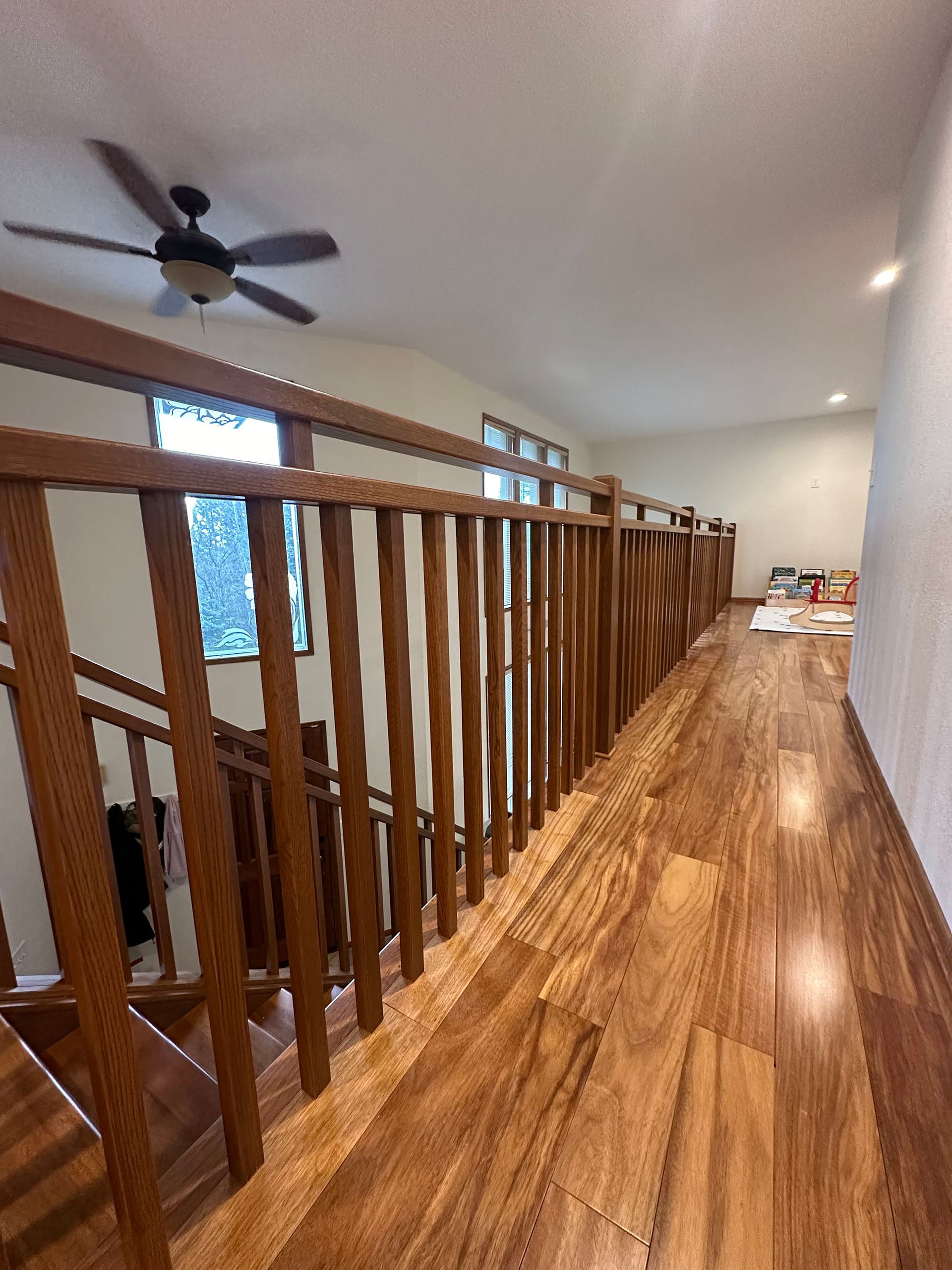 A hallway with a wooden railing and a ceiling fan.