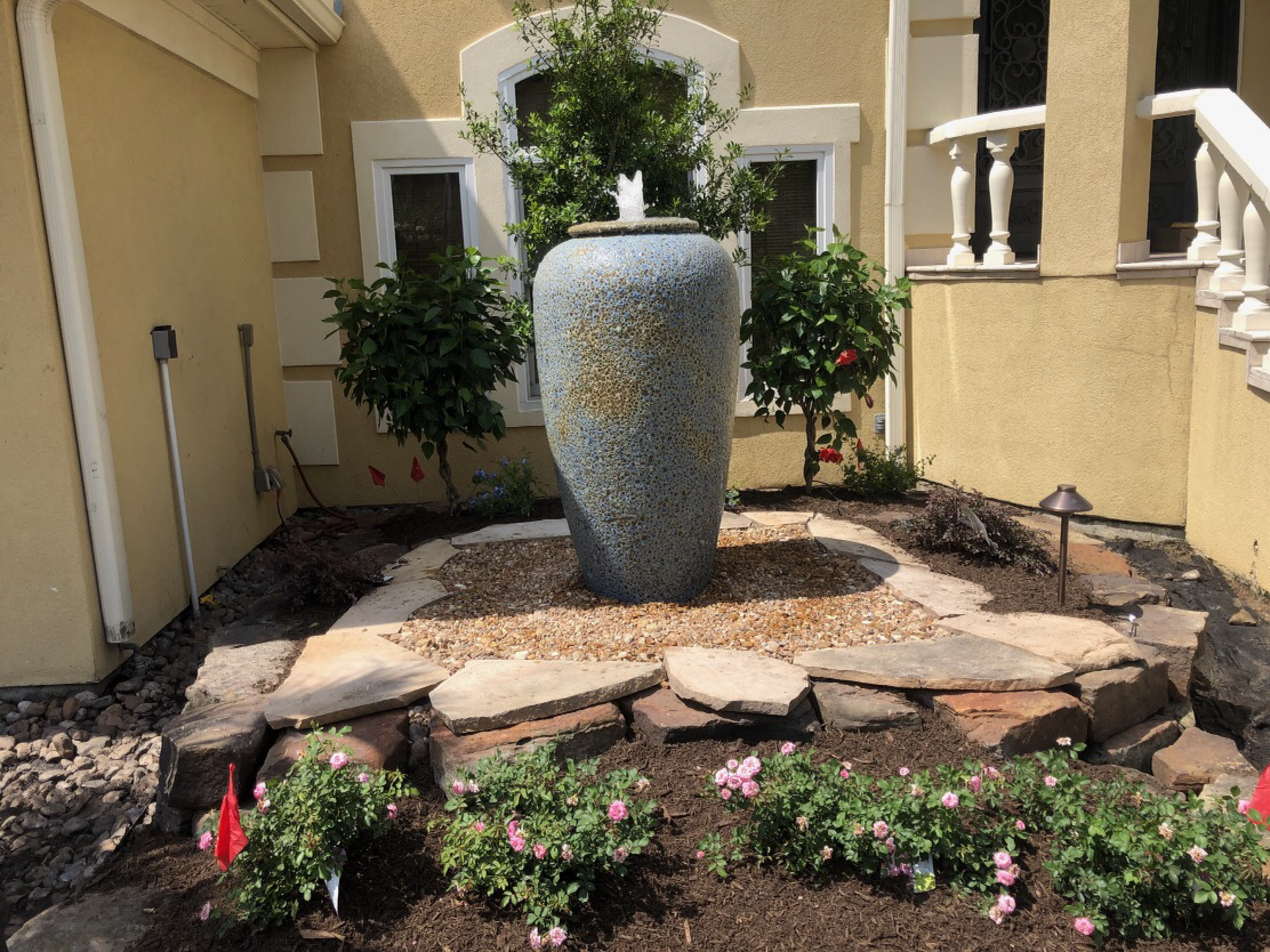 A decorative water fountain surrounded by a rock border and flower garden.