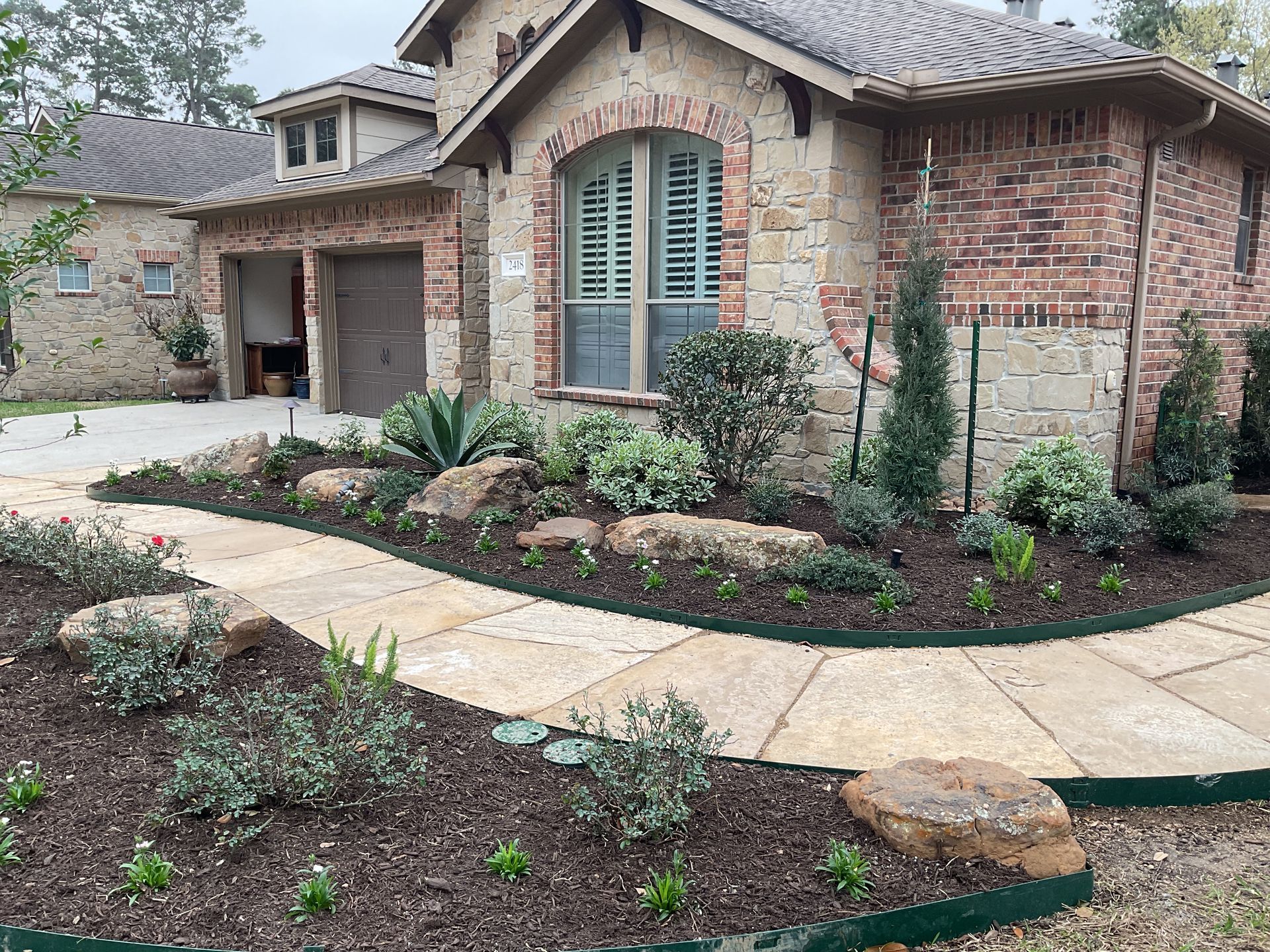 Stone pathway winds past a landscaped front yard with a beige brick house.