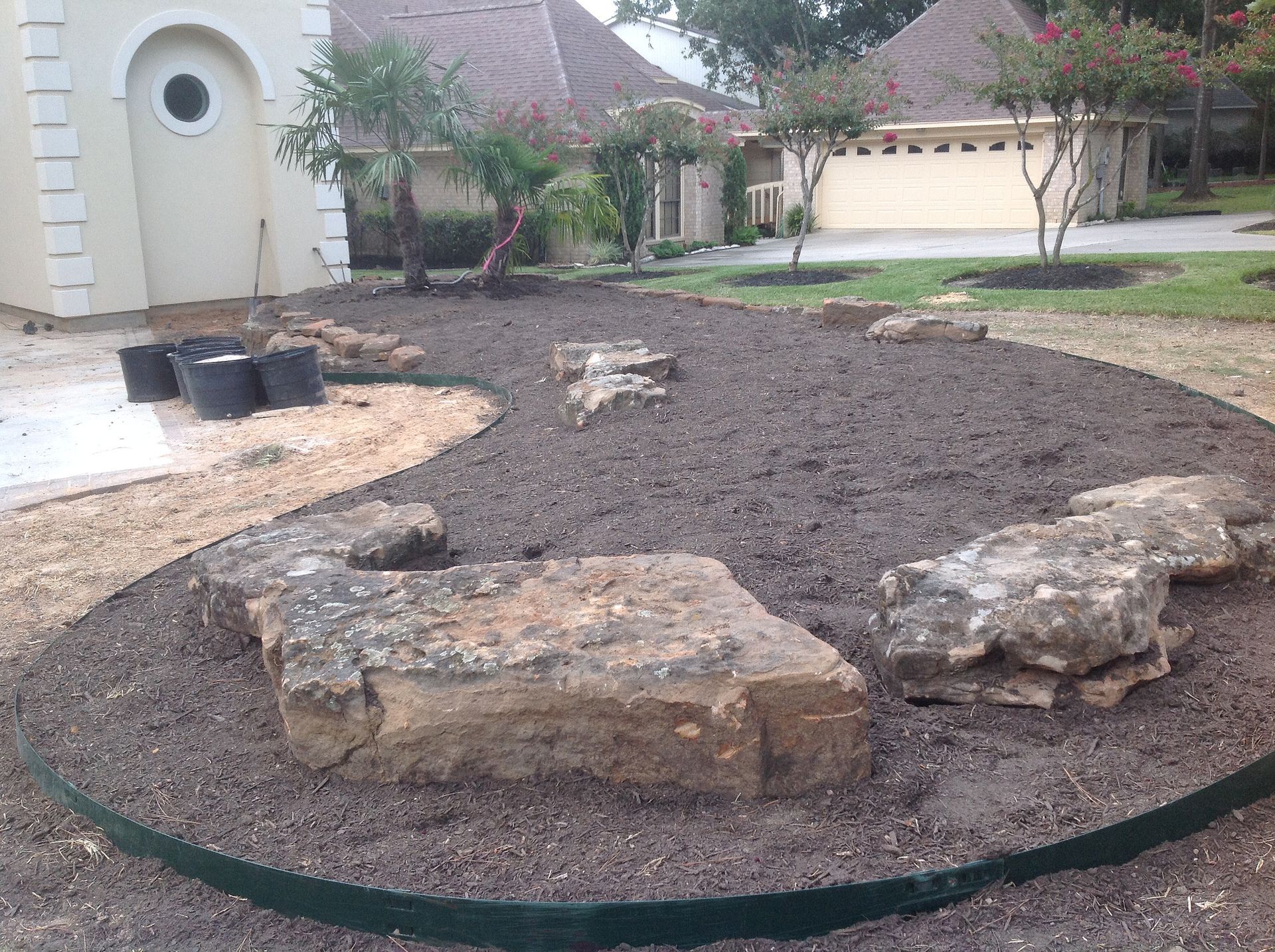 A newly mulched garden bed with large rocks and edging in front of a house.