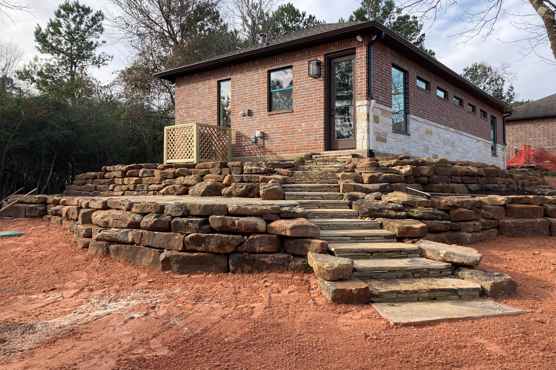 Brick building with stone steps and retaining walls; red dirt yard.