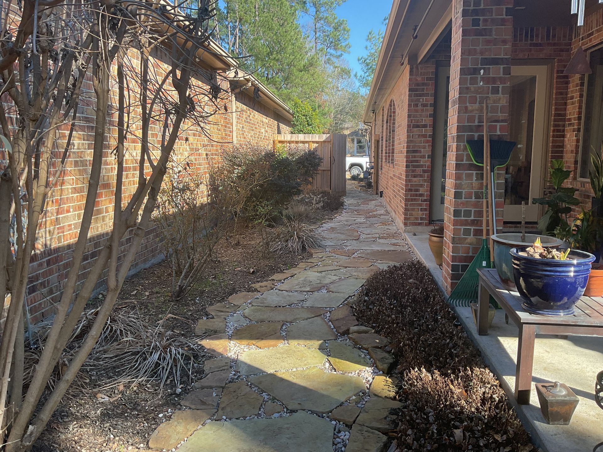Stone path between brick buildings; plants along path, clear sky visible.