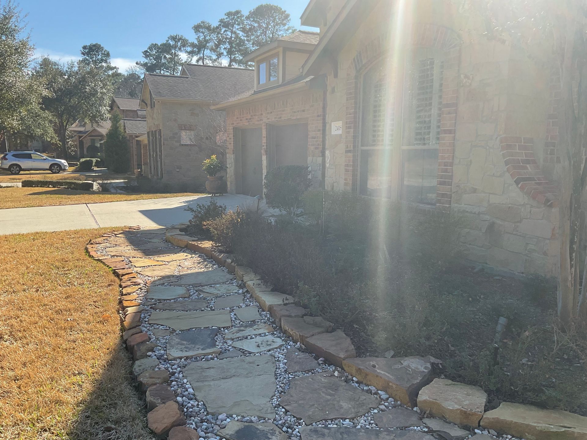 Stone pathway leads to a brick house with sunlight shining.