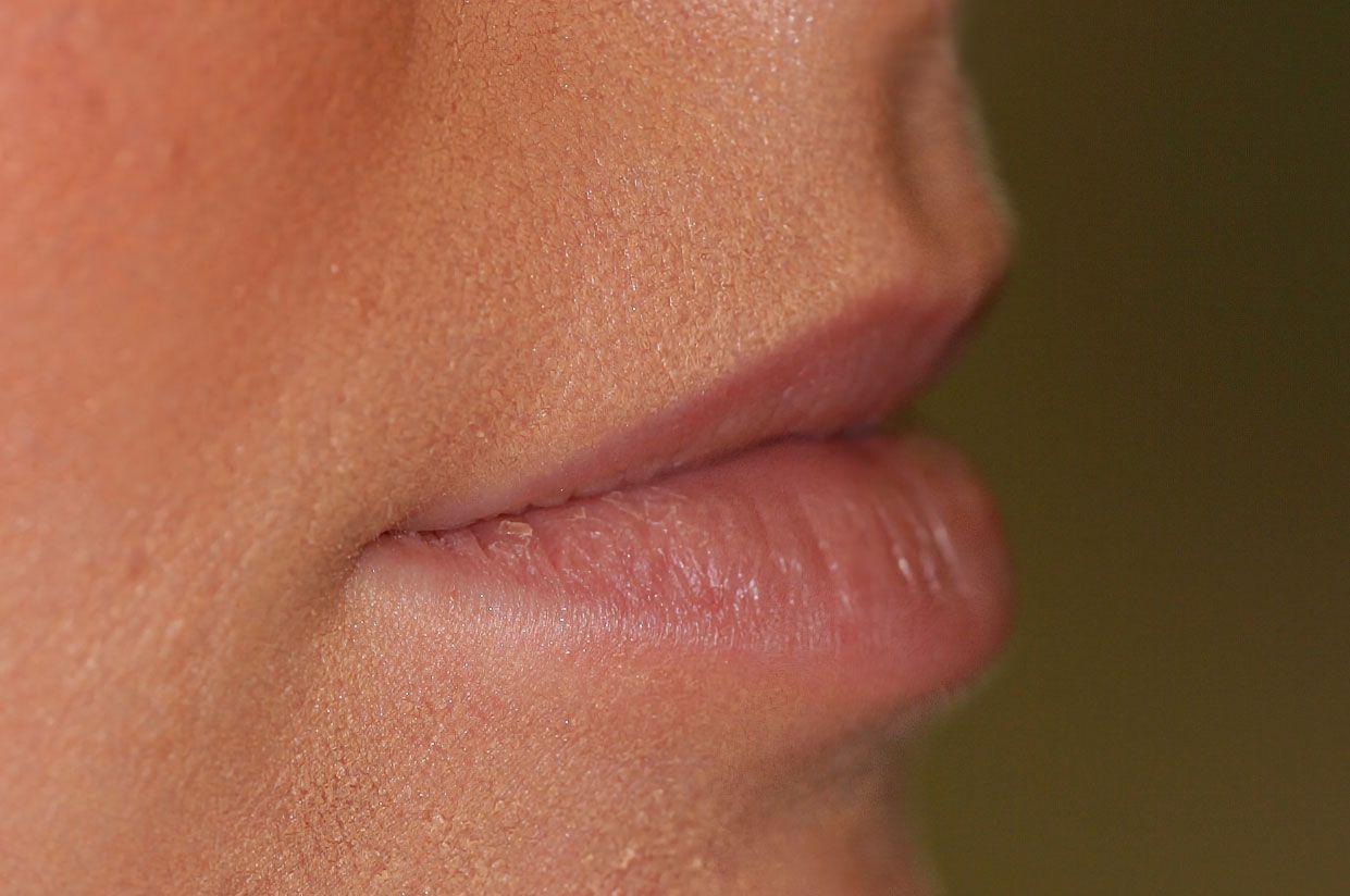 Close-up side view of a person's slightly parted, light pink lips against peachy skin.