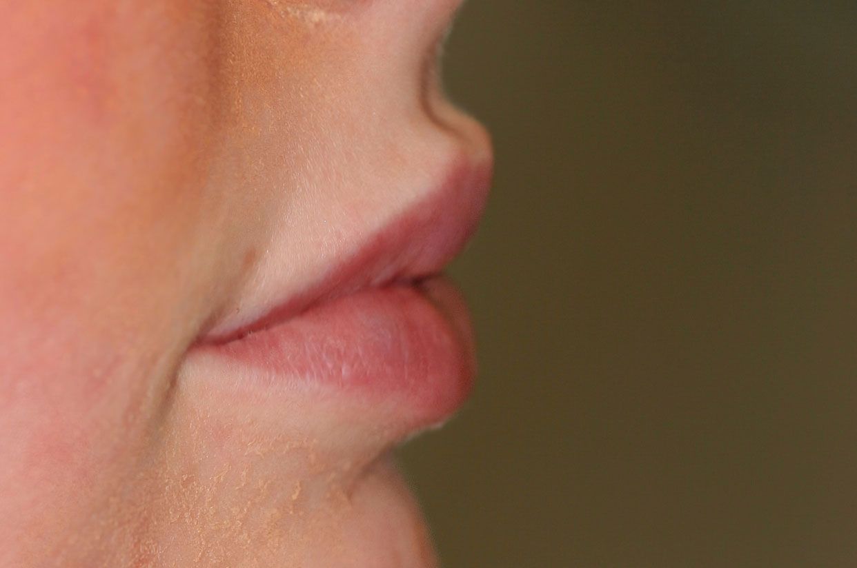 Close-up side view of a person's slightly parted lips, pale pink and defined.