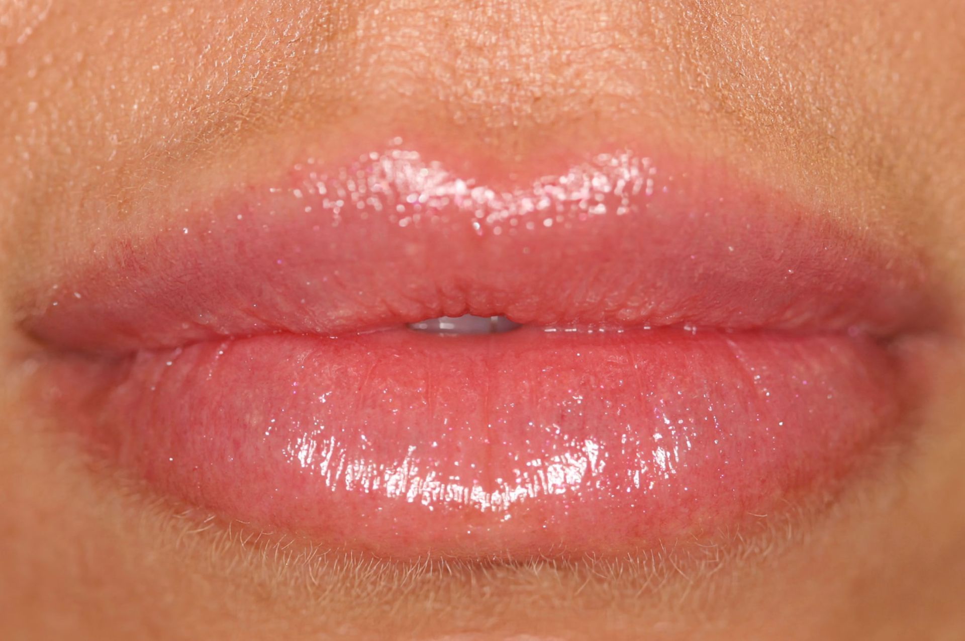 Close-up of full, glossy pink lips, with a soft shine reflecting light.