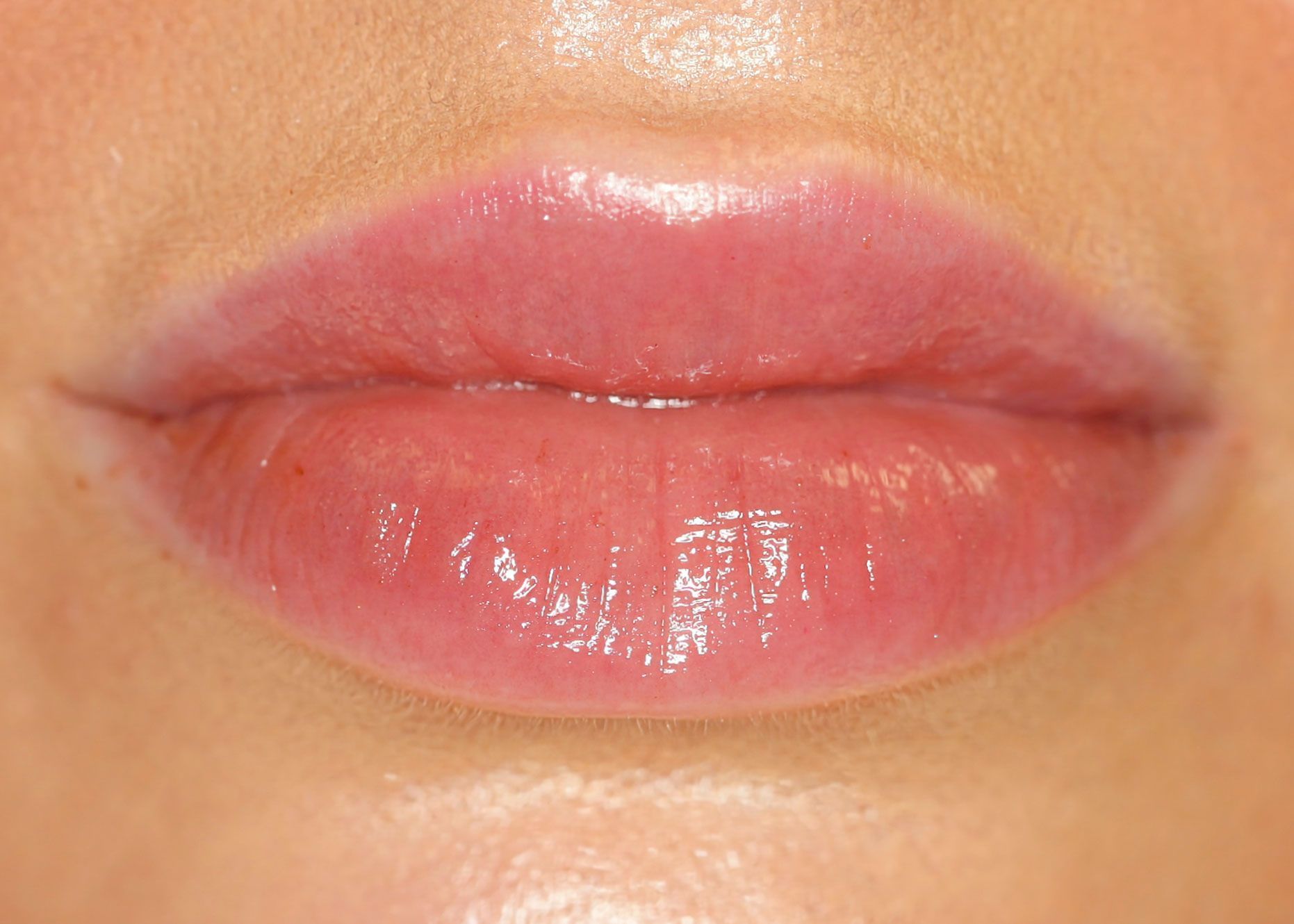 A close-up view of a person's mouth with glossy, pink-toned lips slightly parted.