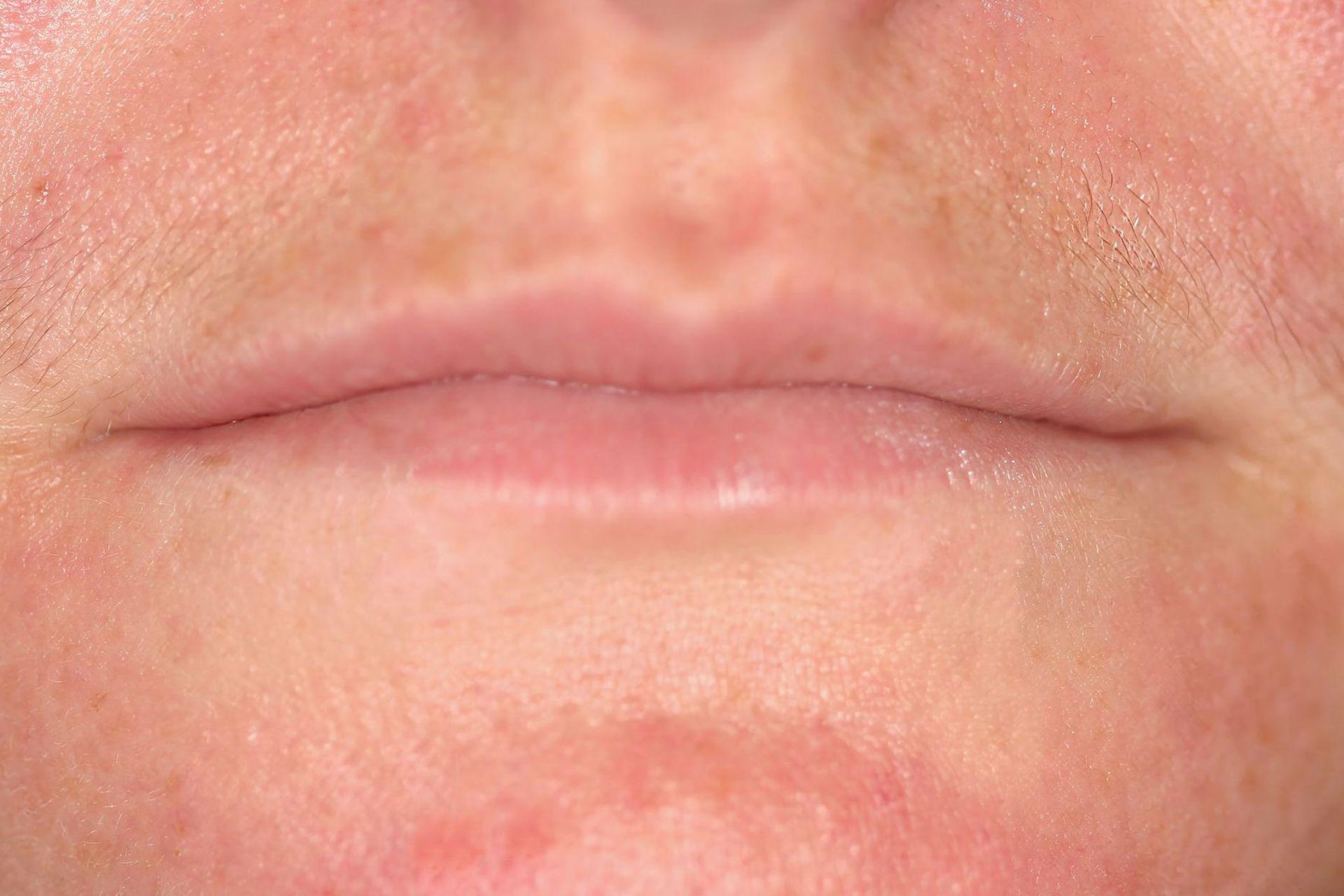 Close-up of a person's lips. The lips are closed and slightly pink, with fine lines around the mouth.