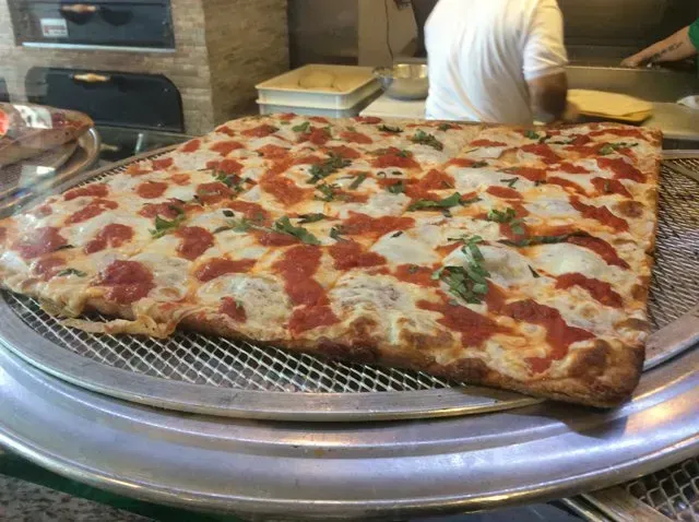 A large slice of pizza is sitting on a metal tray.