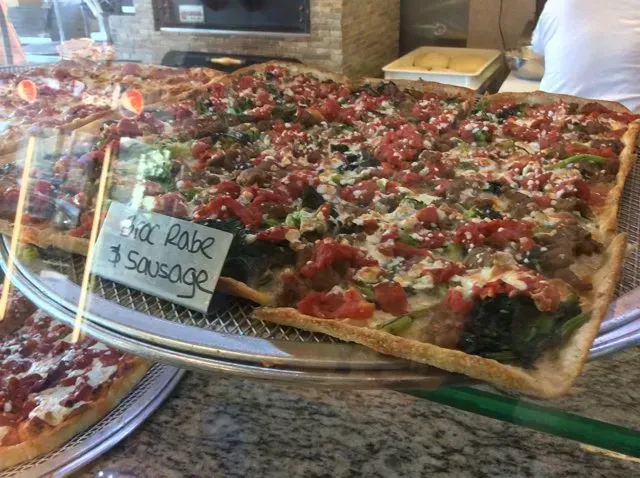 A pizza with tomatoes , peppers , and sausage is sitting on a tray in a restaurant.