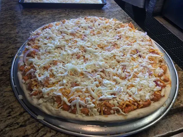 A pizza with cheese on top of it is on a pan on a counter.