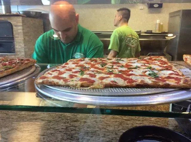 A man in a green shirt is looking at a pizza on a tray.