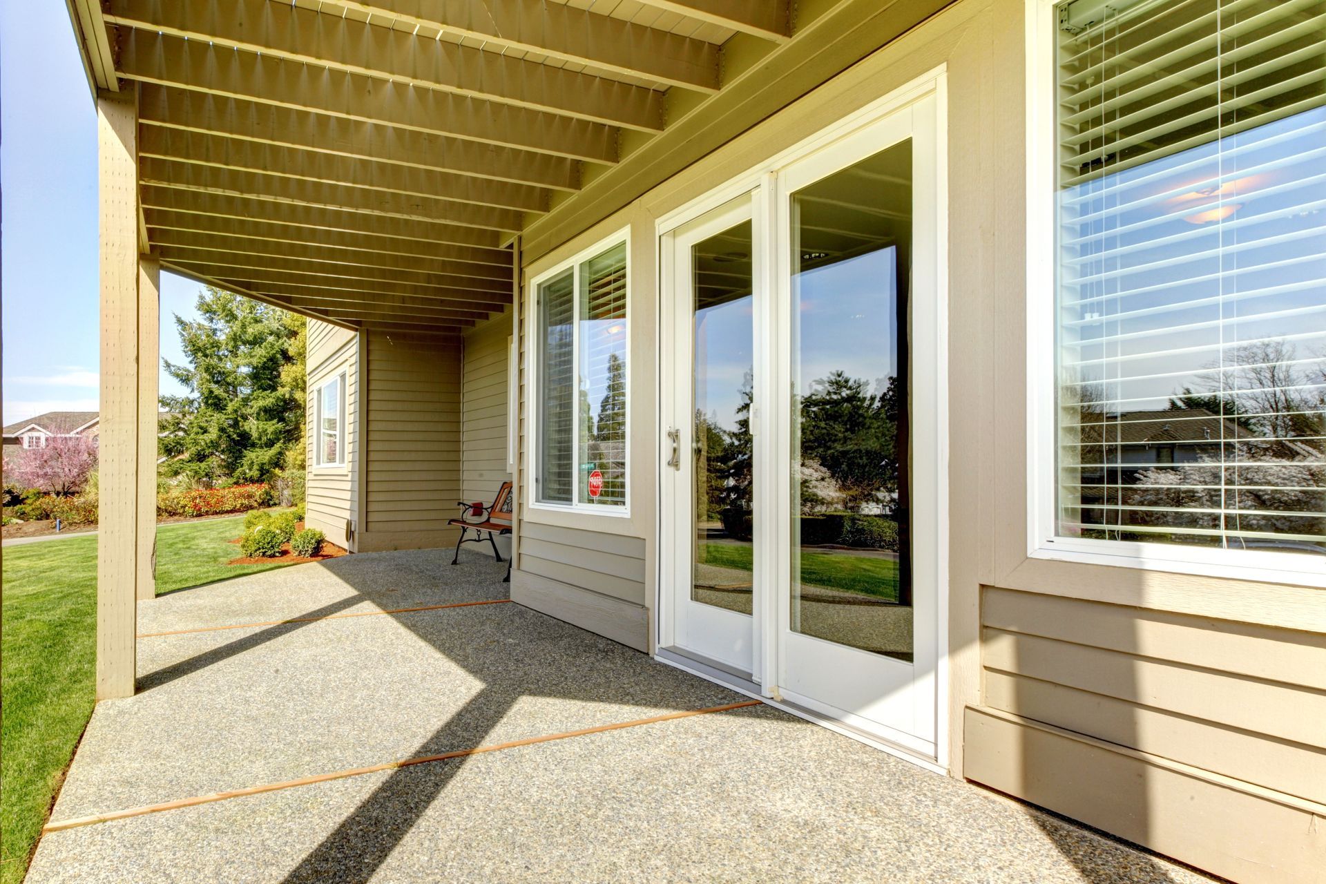 Covered patio with beige siding, white French doors, and sunlit concrete floor.