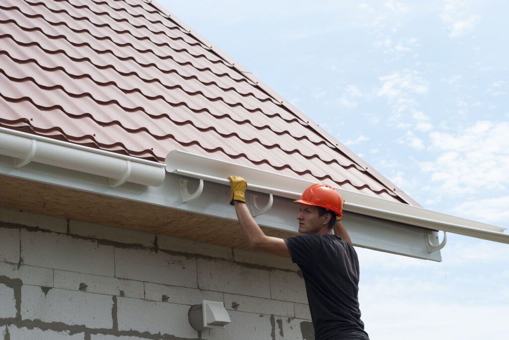 A man is installing a gutter on the side of a house.