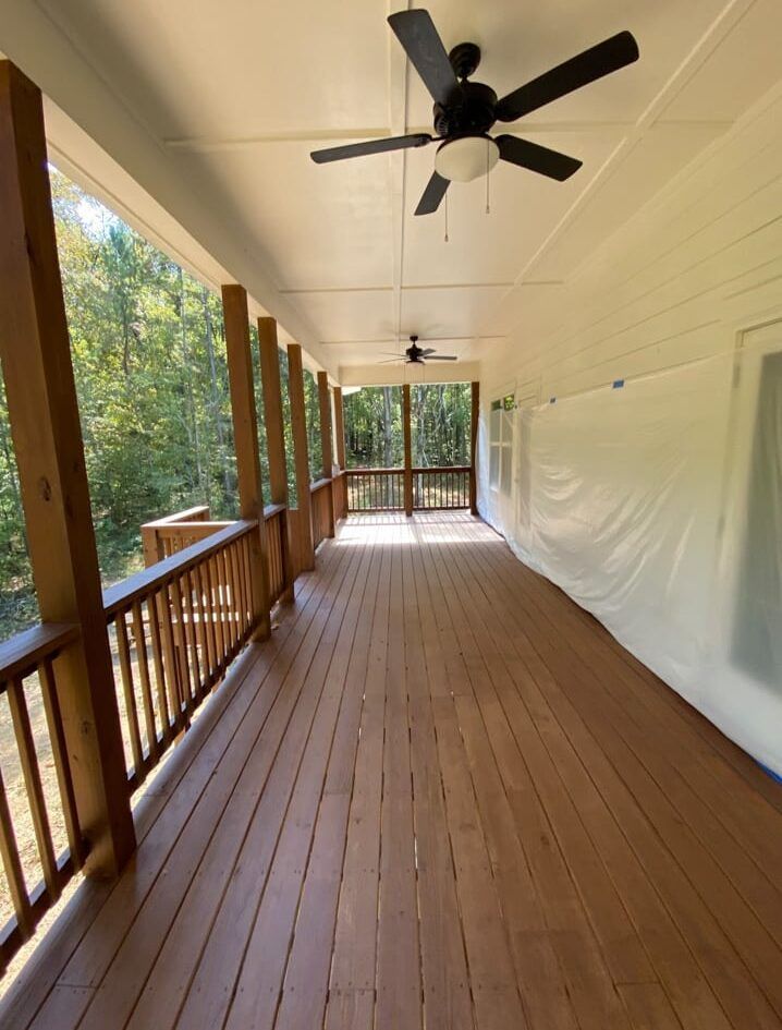 Wooden porch with dark stain, brown posts, black ceiling fans, and surrounding trees.