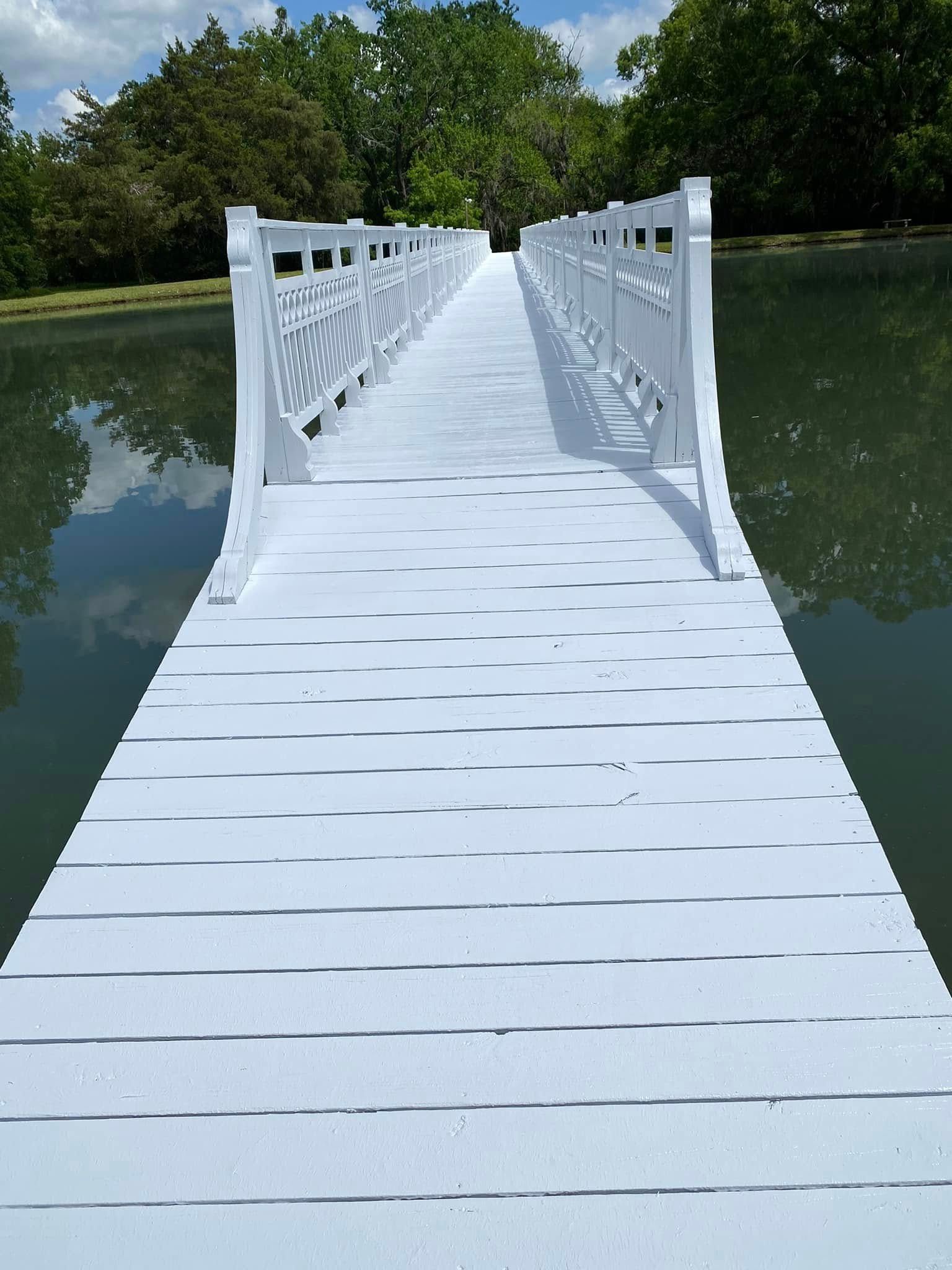 White bridge over calm water, surrounded by trees under a blue sky.