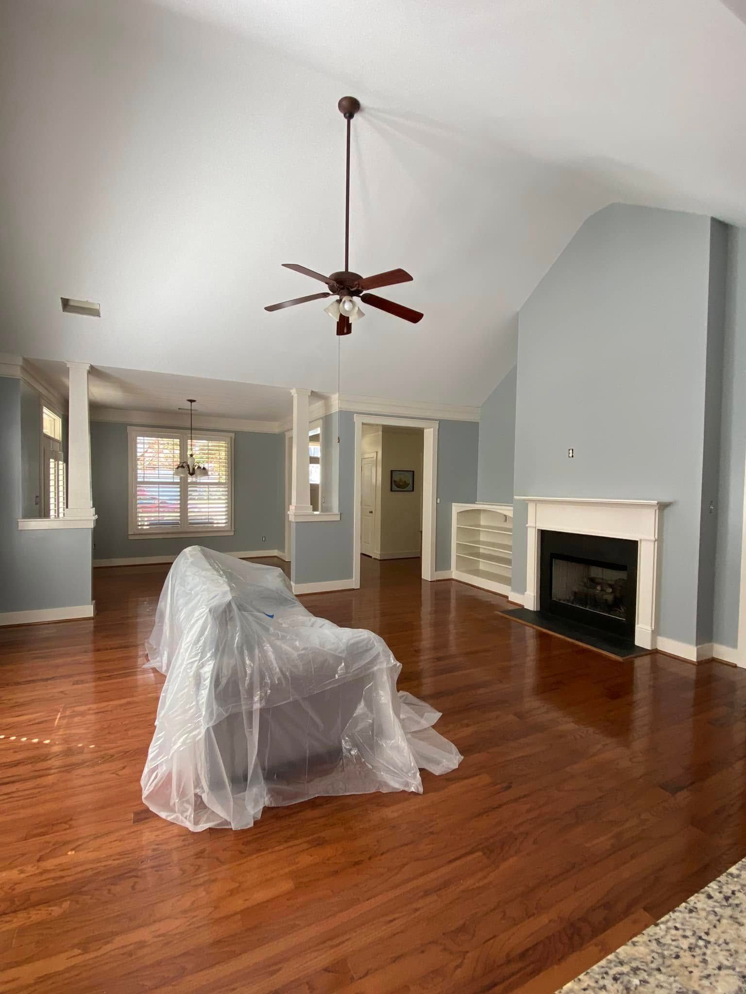 Spacious living room with hardwood floors, blue walls, fireplace, covered furniture, and a ceiling fan.