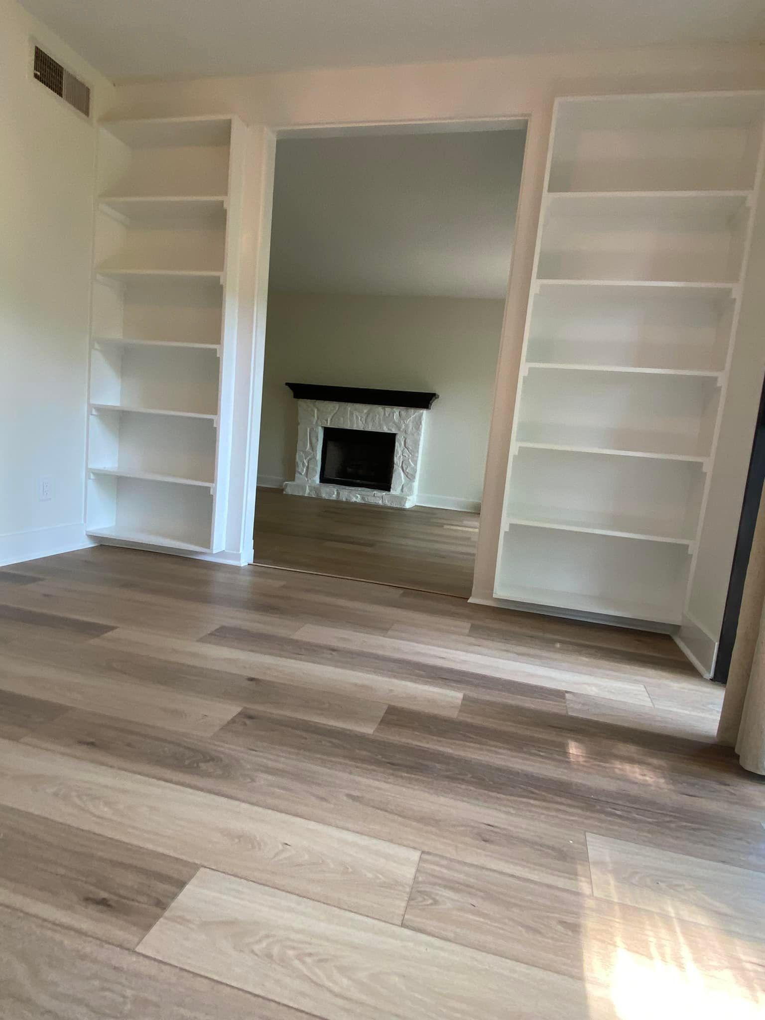 Built-in white bookshelves frame an opening into a living room with a fireplace and wood floors.