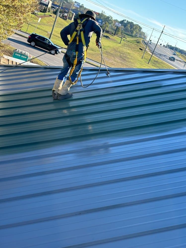 Person in safety gear on a green metal roof, working near a road with a car.