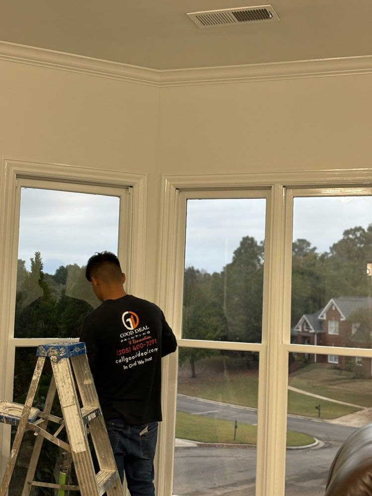 Man applying window tint in a room with a view of a neighborhood. He is standing on a ladder.