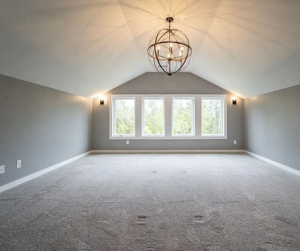 A spacious, gray-walled room with carpet and a chandelier, a row of windows at the far end.