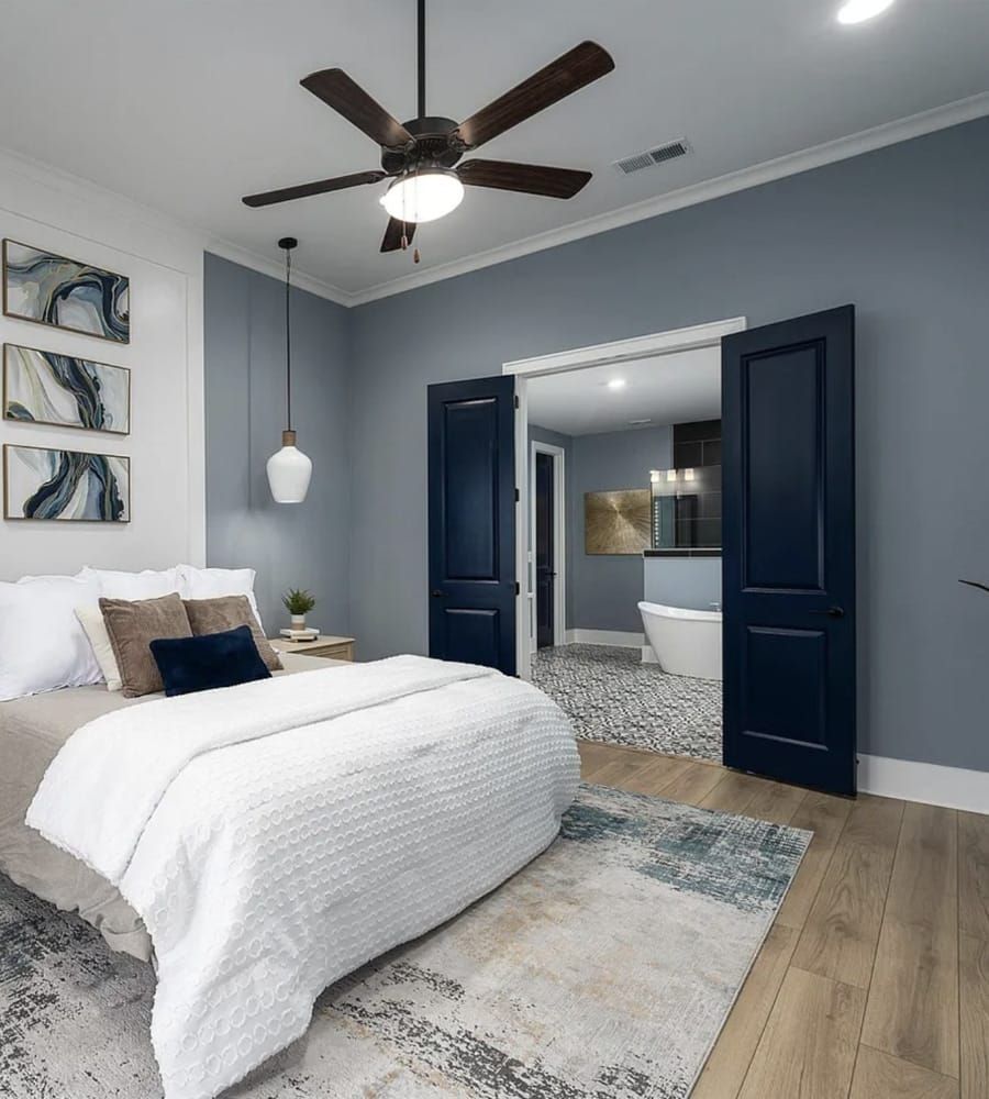Bedroom with blue walls, dark blue doors, white bedding, and a view of the bathroom.