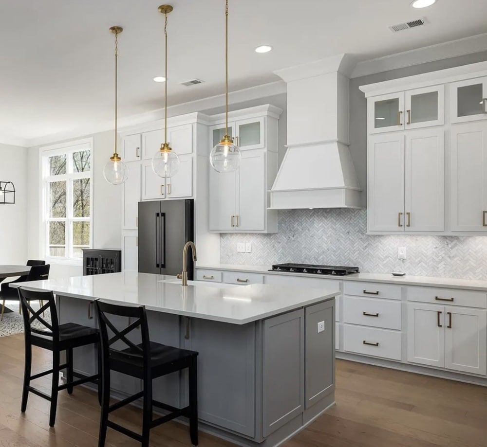 Modern kitchen with white cabinets, gray island, and black stools.