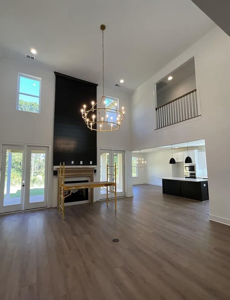 Spacious, modern living room with high ceilings, large chandelier, black fireplace, and hardwood floors.