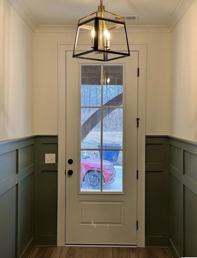 Entryway with olive green wainscoting, cream walls, glass-paned door, and hanging light fixture.
