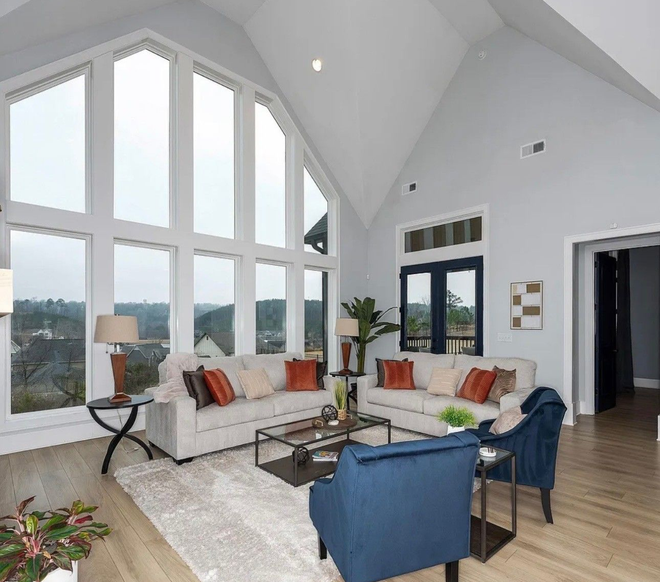 Living room with large windows overlooking a landscape, two couches, and blue accent chairs.