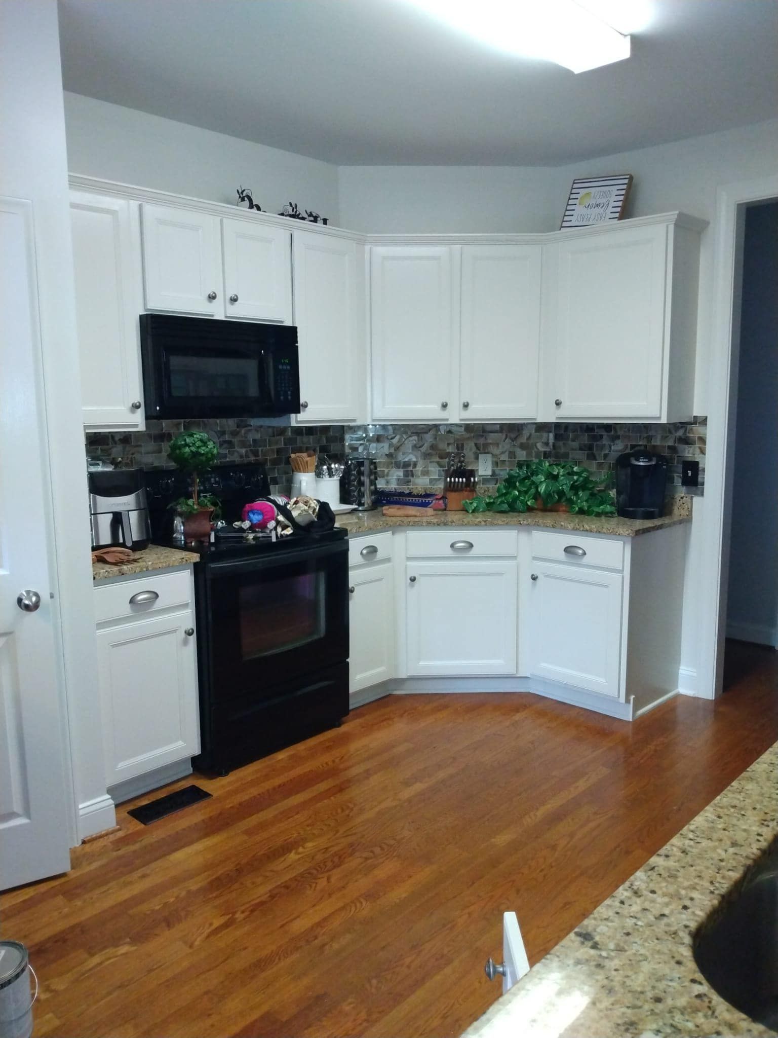 White kitchen with black appliances, wood floors, and granite countertops.