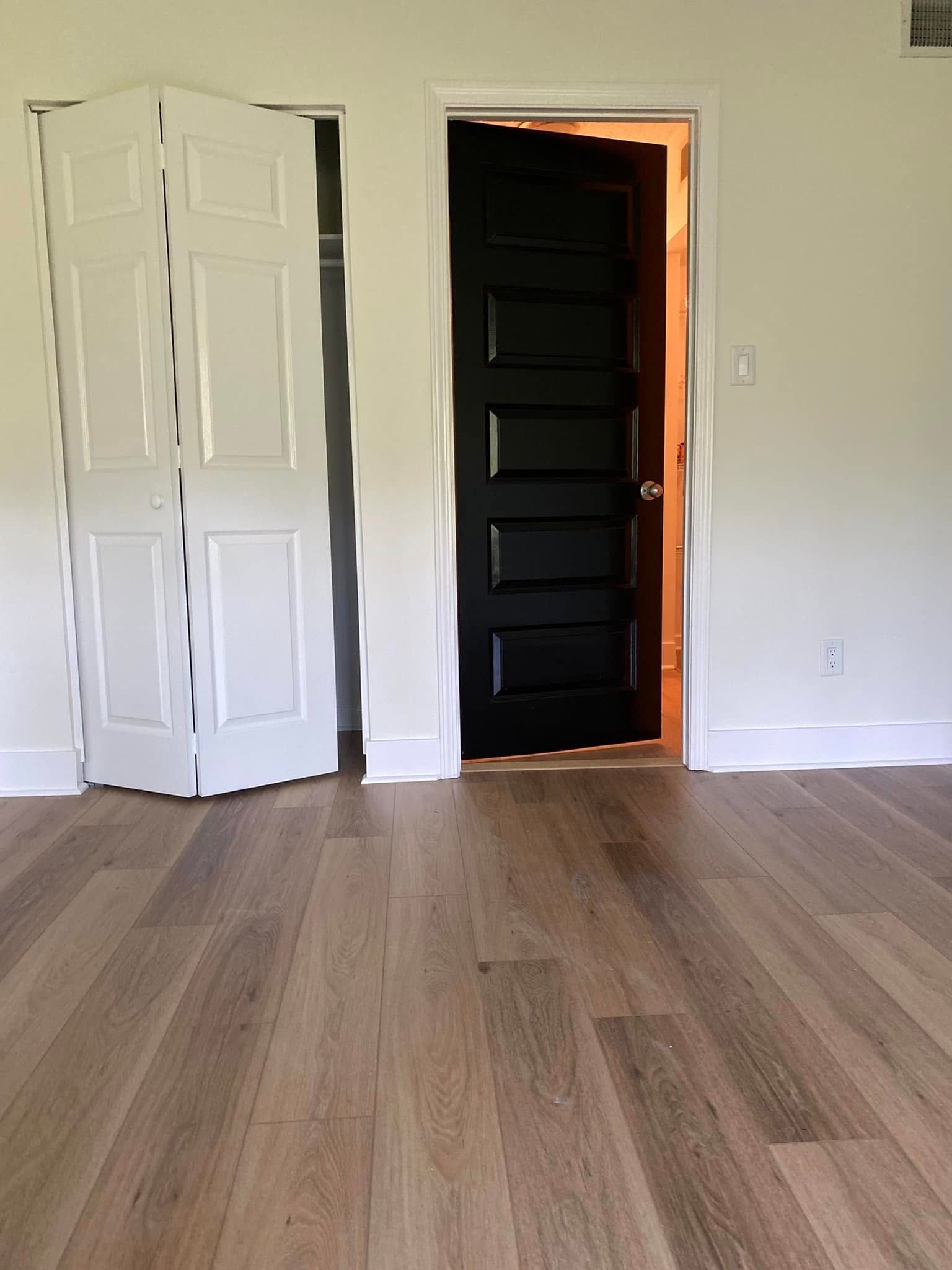 A room with white walls, hardwood floor, a white bi-fold closet door, and a black door.