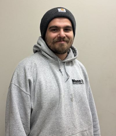Man with a beard wearing a gray Carhartt beanie and a gray hooded sweatshirt, standing in front of a neutral wall.