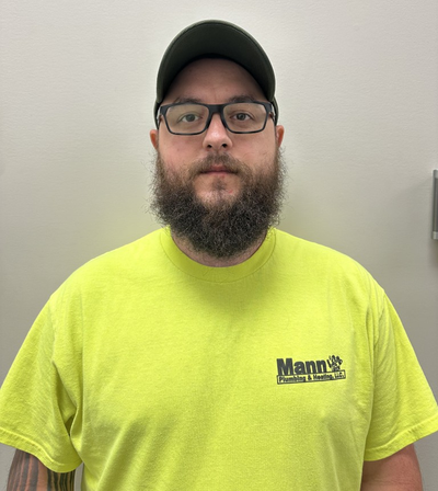 Man with glasses, beard, and cap in a green work shirt, standing against a neutral wall.
