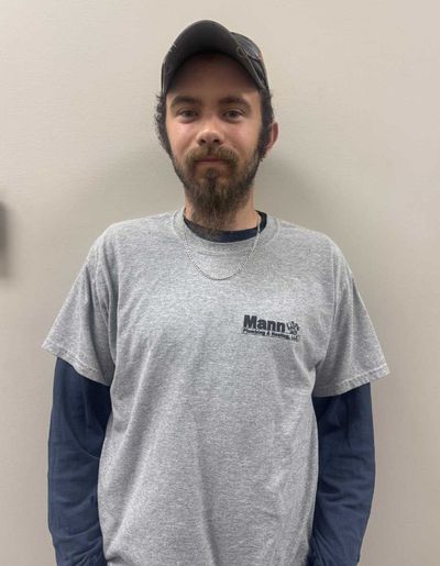 Man in gray t-shirt and baseball cap stands against a plain wall. He has a beard and looks directly at the camera.