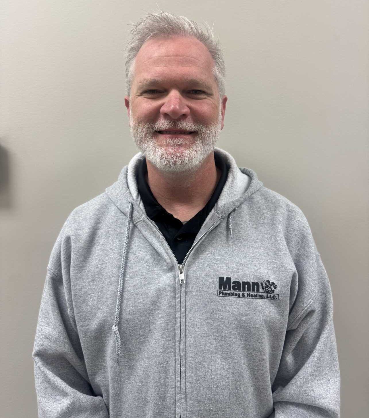 Man in gray zip-up hoodie, smiling, in front of a neutral wall. 