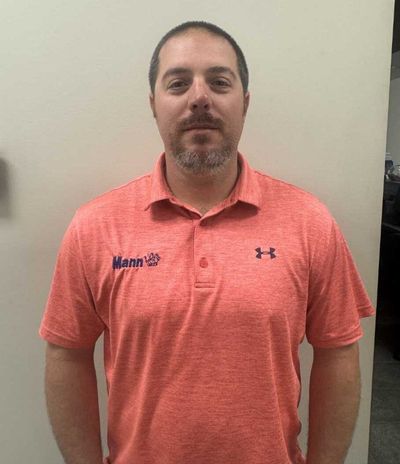 Man in red polo shirt, arms at sides, standing in front of a neutral wall.