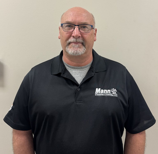 Man wearing glasses and a black polo shirt, standing in front of a neutral wall.