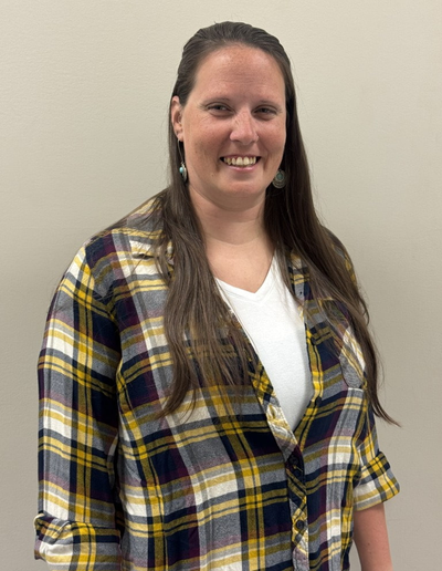 Woman smiling, wearing a white shirt and plaid button-up, standing in front of a neutral wall.