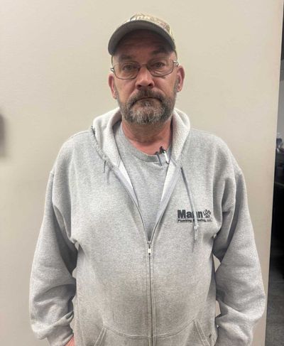 Man in gray hoodie and hat, wearing glasses, standing in a room.