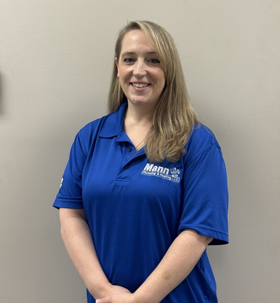 Woman wearing a blue polo shirt, smiling, standing in front of a neutral wall.