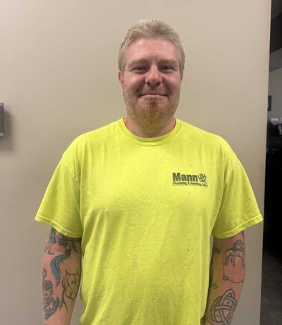 Man in a yellow shirt with tattoos, standing indoors, smiling.