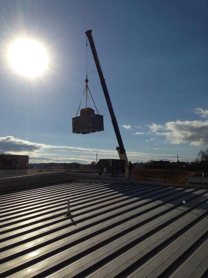 A crane lifts a large object over a corrugated metal roof under a bright sun.