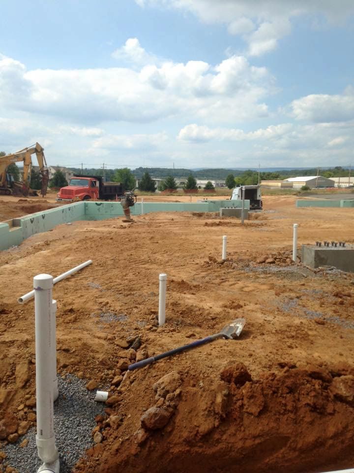 Construction site with foundation, pipes, dirt, and equipment under a cloudy sky.