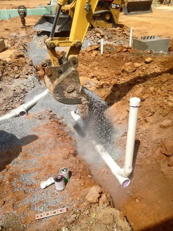 Excavator digging trench around white PVC pipes, construction site.