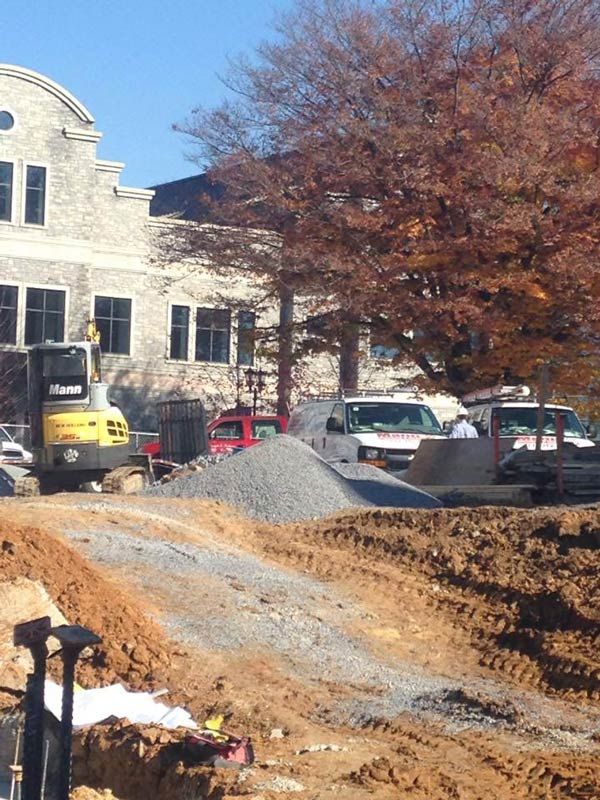 Construction site with excavator and pile of gravel in front of a building with fall foliage.
