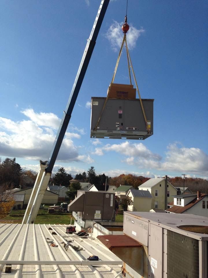 A crane lifts an HVAC unit onto a rooftop. Blue sky with white clouds.