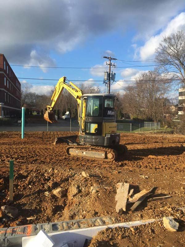 Yellow excavator on dirt, clearing land near buildings under a blue sky.