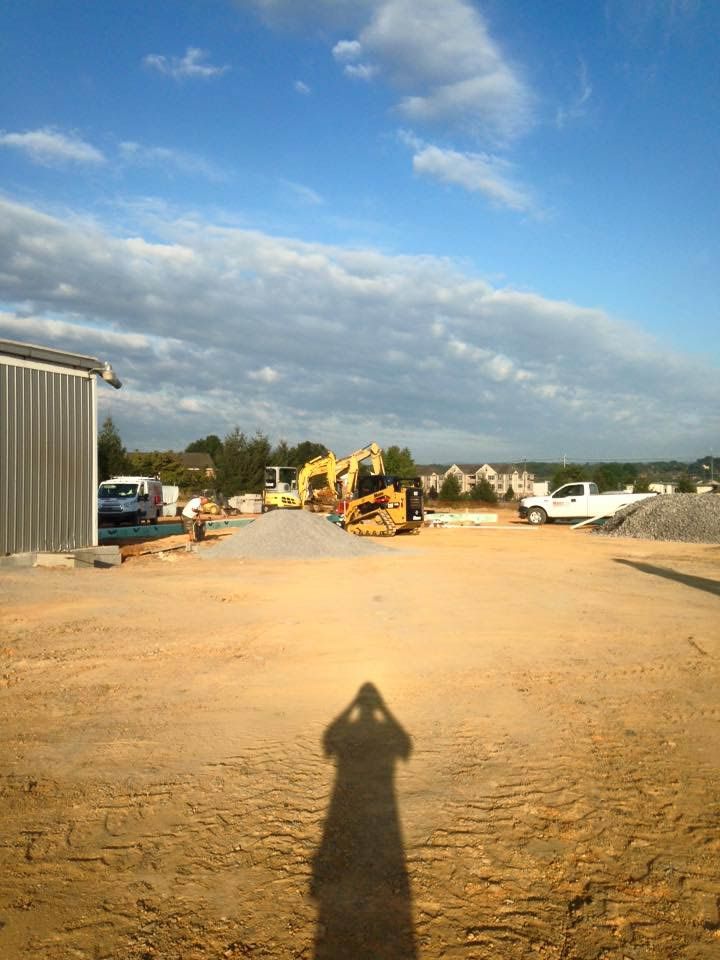 Construction site, shadow of person, heavy equipment, gravel lot, cloudy sky.